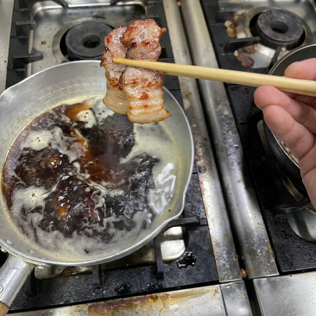 Un morceau de poitrine de porc cuit et doré tenu par des baguettes au-dessus dune casserole de sauce frémissante.