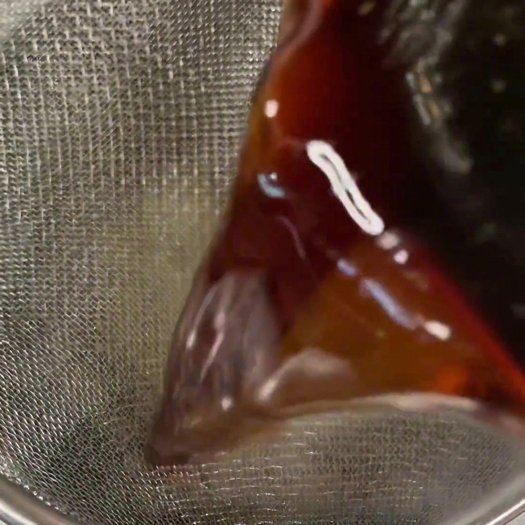 Gros plan dune sauce sombre et translucide versée à travers une passoire à mailles fines.