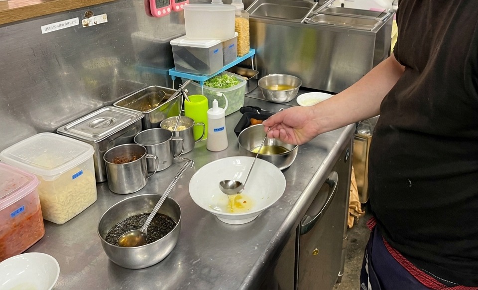 Une louche versant une huile dorée et claire dans un bol en céramique blanche sur un comptoir en inox.