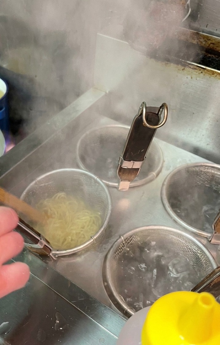 Nouilles cuisant dans une passoire en maille immergée dans une eau bouillante bouillonnante.