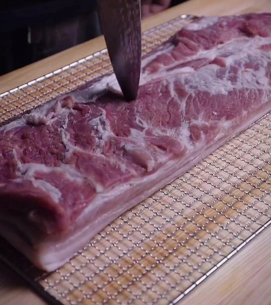 Gros plan de la pointe dun couteau perçant de petits trous dans la surface de la poitrine de porc crue.
