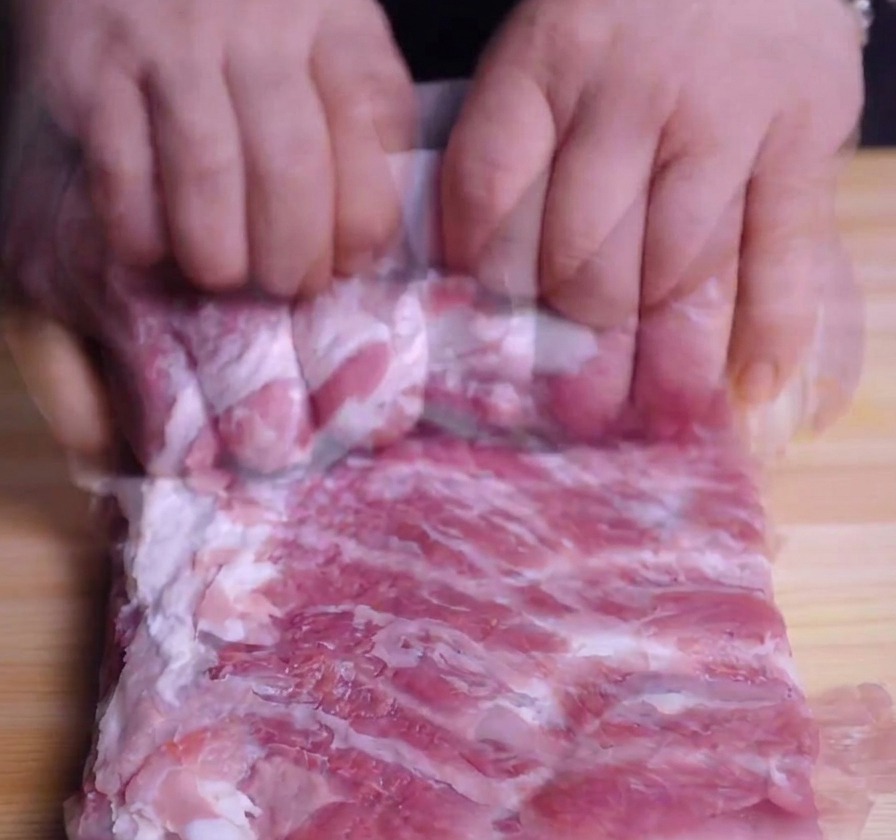 Mains en train de rouler fermement une poitrine de porc crue en cylindre sur une planche à découper.