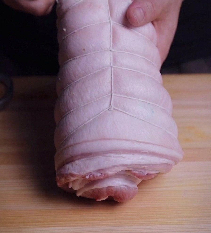 Mains tenant un rouleau de poitrine de porc tout en lattachant avec de la ficelle de cuisine blanche.