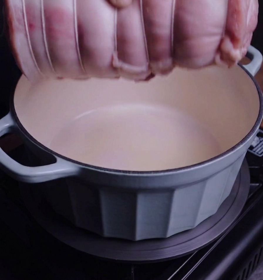 Un rouleau de porc ficelé déposé délicatement dans une cocotte en émail bleu clair.