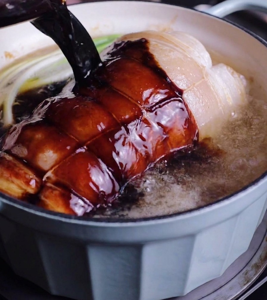 Liquide de braisage sombre versé sur le porc et les oignons verts dans une cocotte bleue.