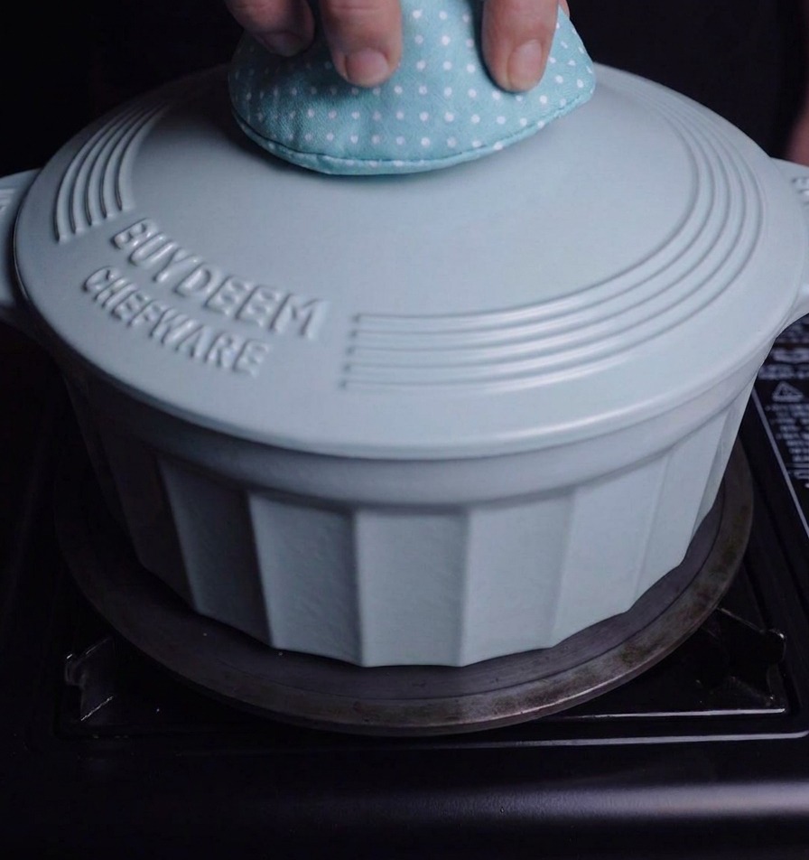 Une personne utilisant un gant de cuisine pour poser le couvercle bleu sur une cocotte assortie sur la cuisinière.