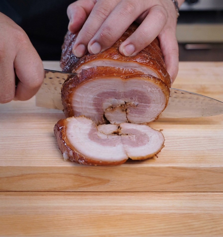 Un chef utilisant un couteau bien aiguisé pour couper des tranches rondes et épaisses dans un billot de chashu froid.