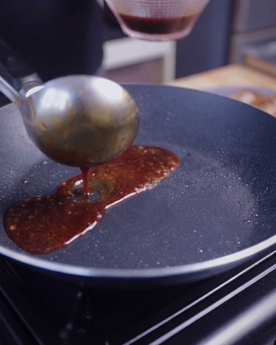 Une louche en métal versant une sauce brune luisante sur des tranches de poitrine de porc grillées.
