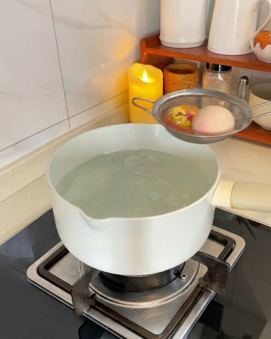 Deux œufs blancs dans une passoire métallique plongés dans une casserole deau bouillante sur une cuisinière.