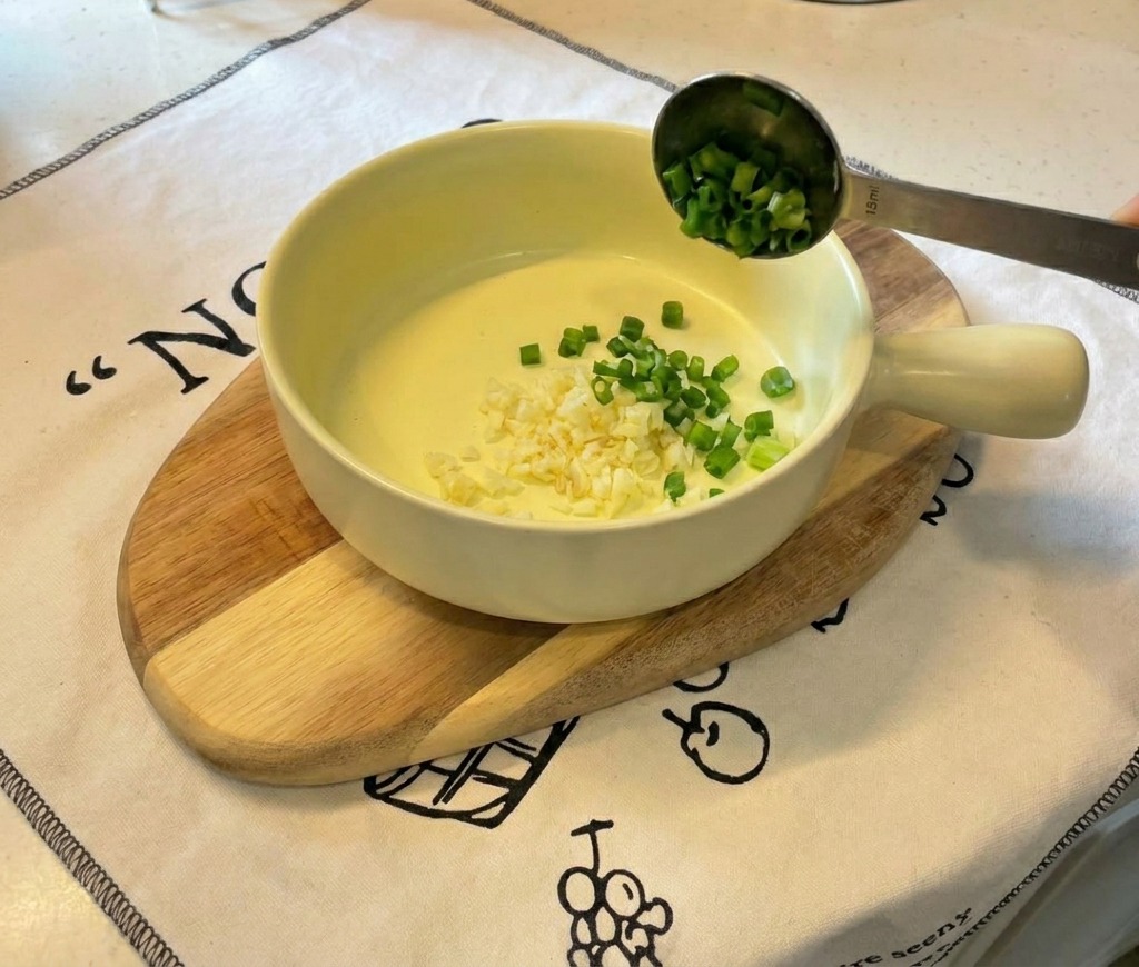 Un petit bol en céramique jaune sur une planche en bois, contenant de lail finement haché et des oignons verts émincés.