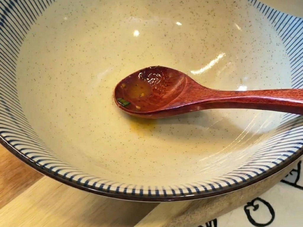 Un bouillon crémeux aux teintes orangées versé depuis un petit bol vers un grand bol de service en céramique rayé bleu et blanc.
