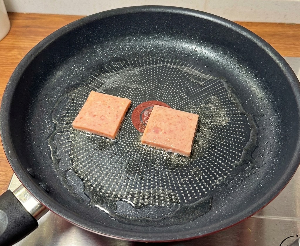 Des tranches de pâté de porc rose saisies dans une poêle noire jusquà ce quelles présentent des marques de grillure dorées.