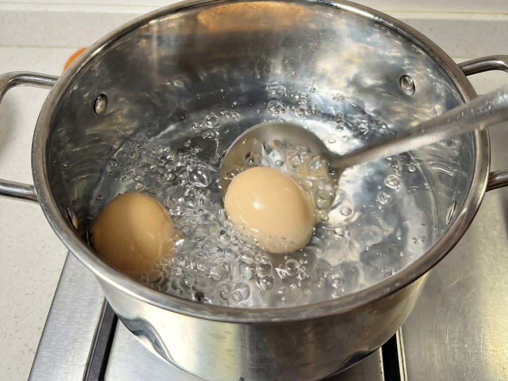 Une écumoire en acier inoxydable sortant deux œufs bruns dune casserole deau bouillante.