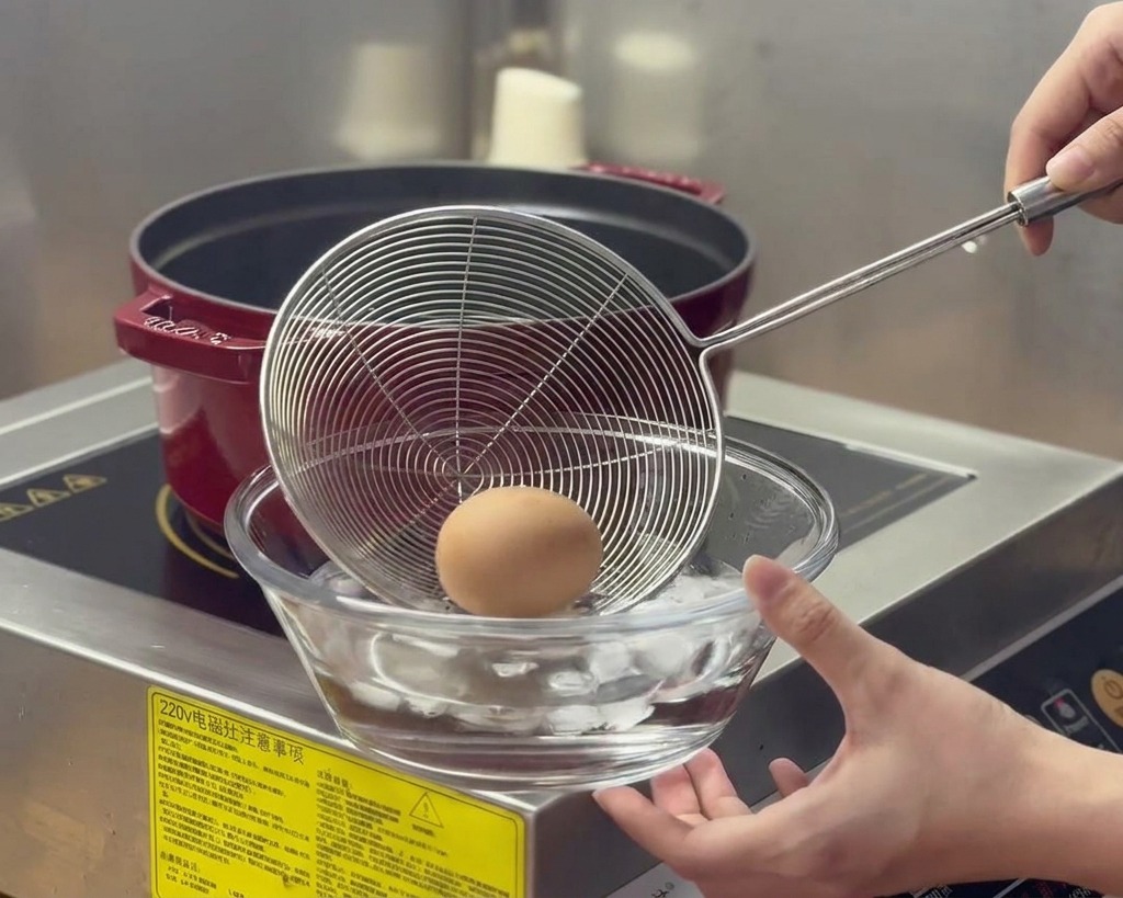 Un œuf bouilli est transféré dune casserole fumante vers un bol en verre rempli deau et de glaçons.
