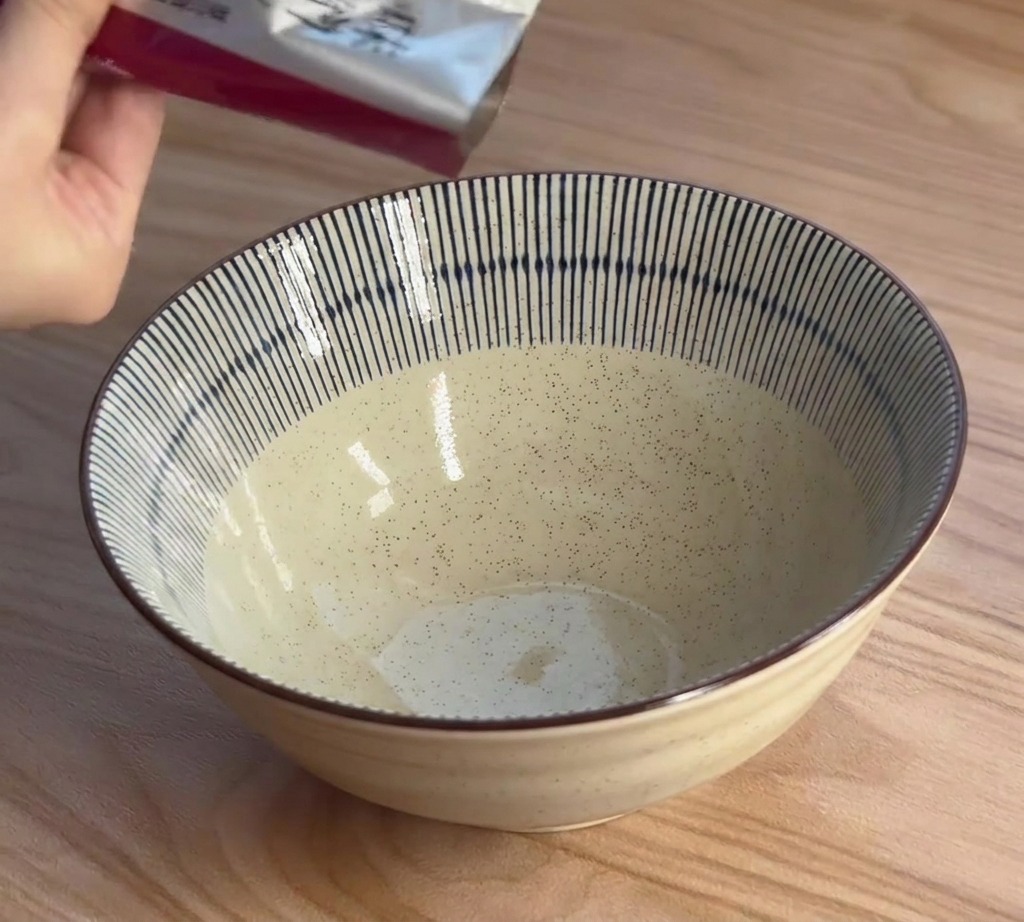 Une main verse la pâte de concentré de miso ramen dun sachet argenté dans un bol en céramique à rayures.