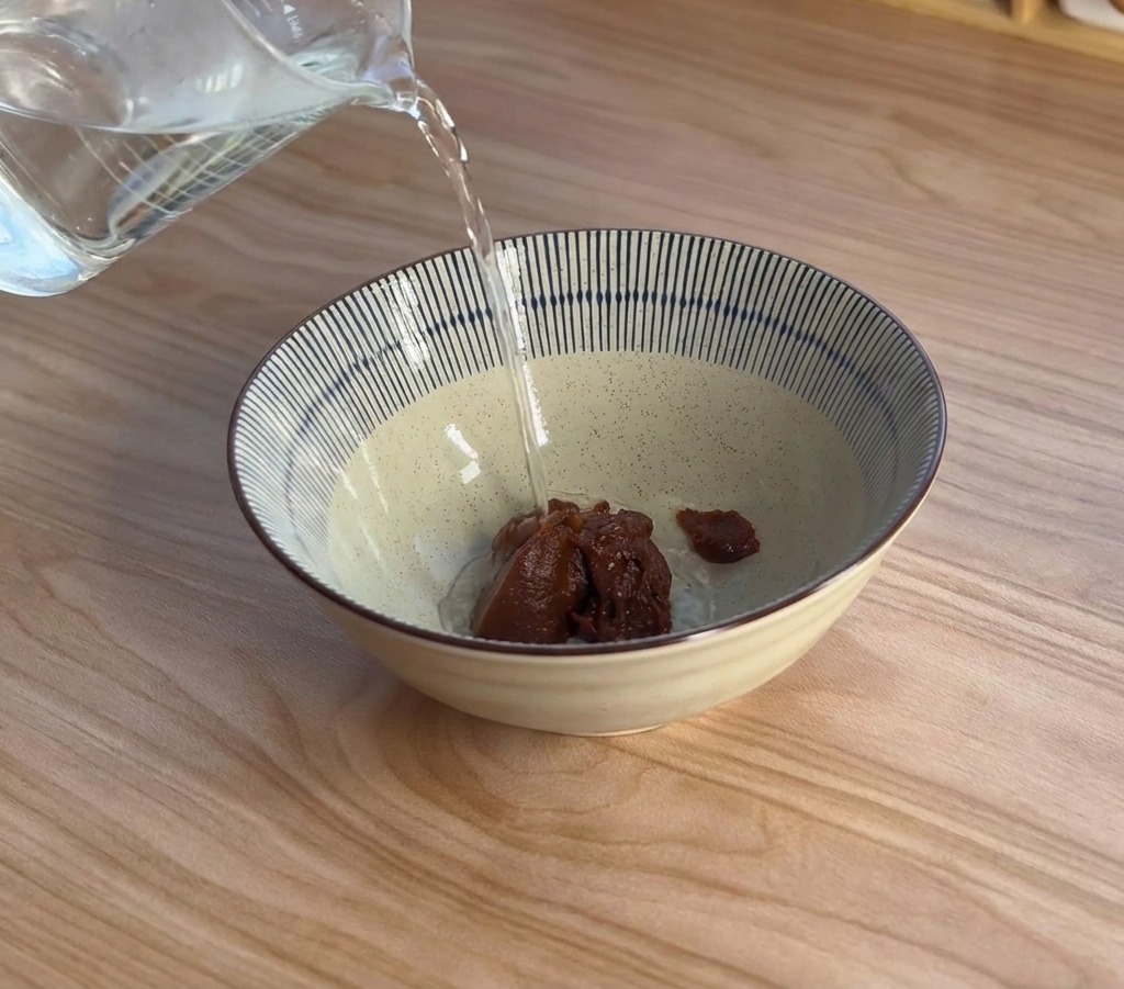 De la vapeur sélève alors que de leau bouillante est versée dun verre doseur dans un bol contenant du concentré de miso.