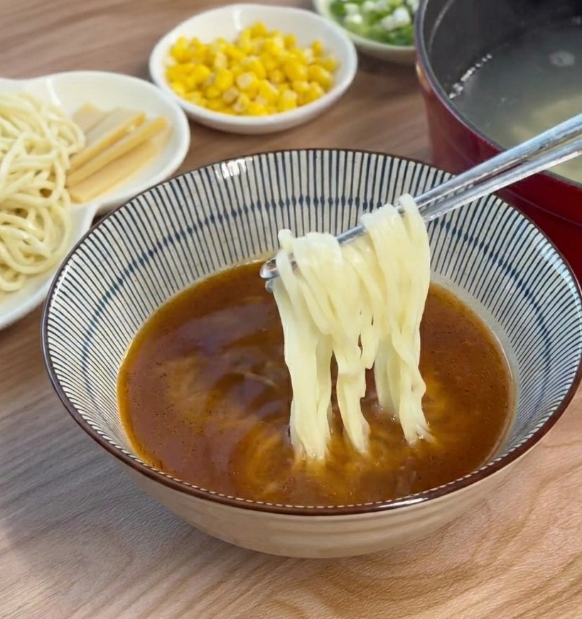 Des nouilles ramen cuites sont mélangées dans un bol de bouillon miso brun à laide de baguettes.