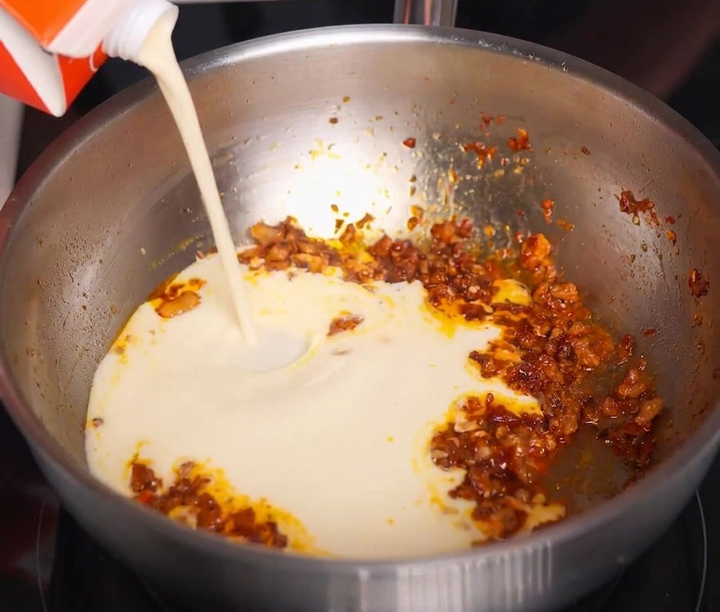 Lait de soja blanc versé dune brique dans la poêle contenant la viande hachée aux épices.