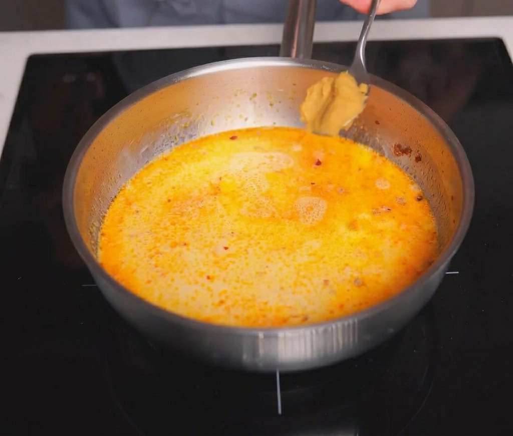 Une cuillerée de pâte miso brun clair ajoutée au bouillon de soupe crémeux et frémissant.