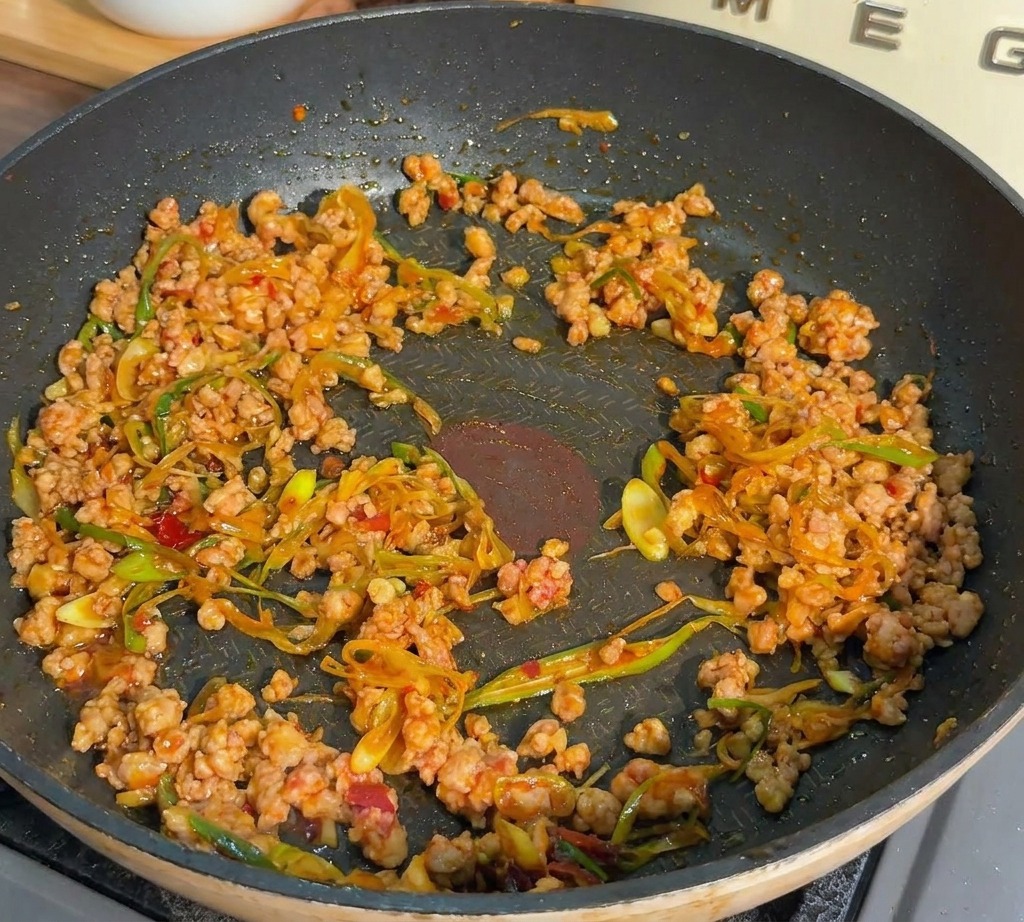 Du porc haché et des oignons verts sautés dans une poêle sombre jusquà ce que la viande soit dorée et cuite.