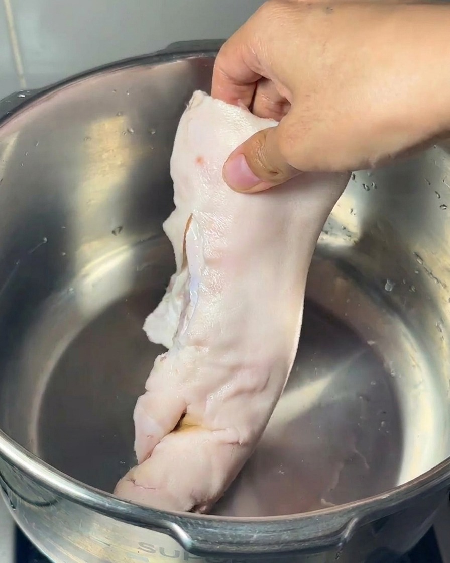 Une main déposant un pied de porc cru, un gros os à moelle et des pattes de poulet dans une cuve en inox.