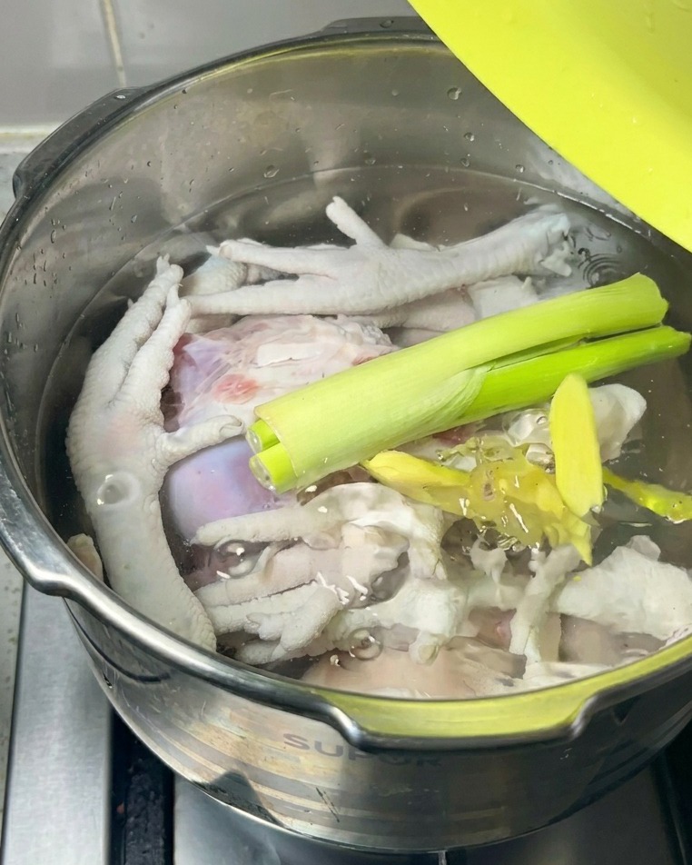 Des oignons verts frais et des tranches de gingembre posés sur la viande crue dans la marmite.