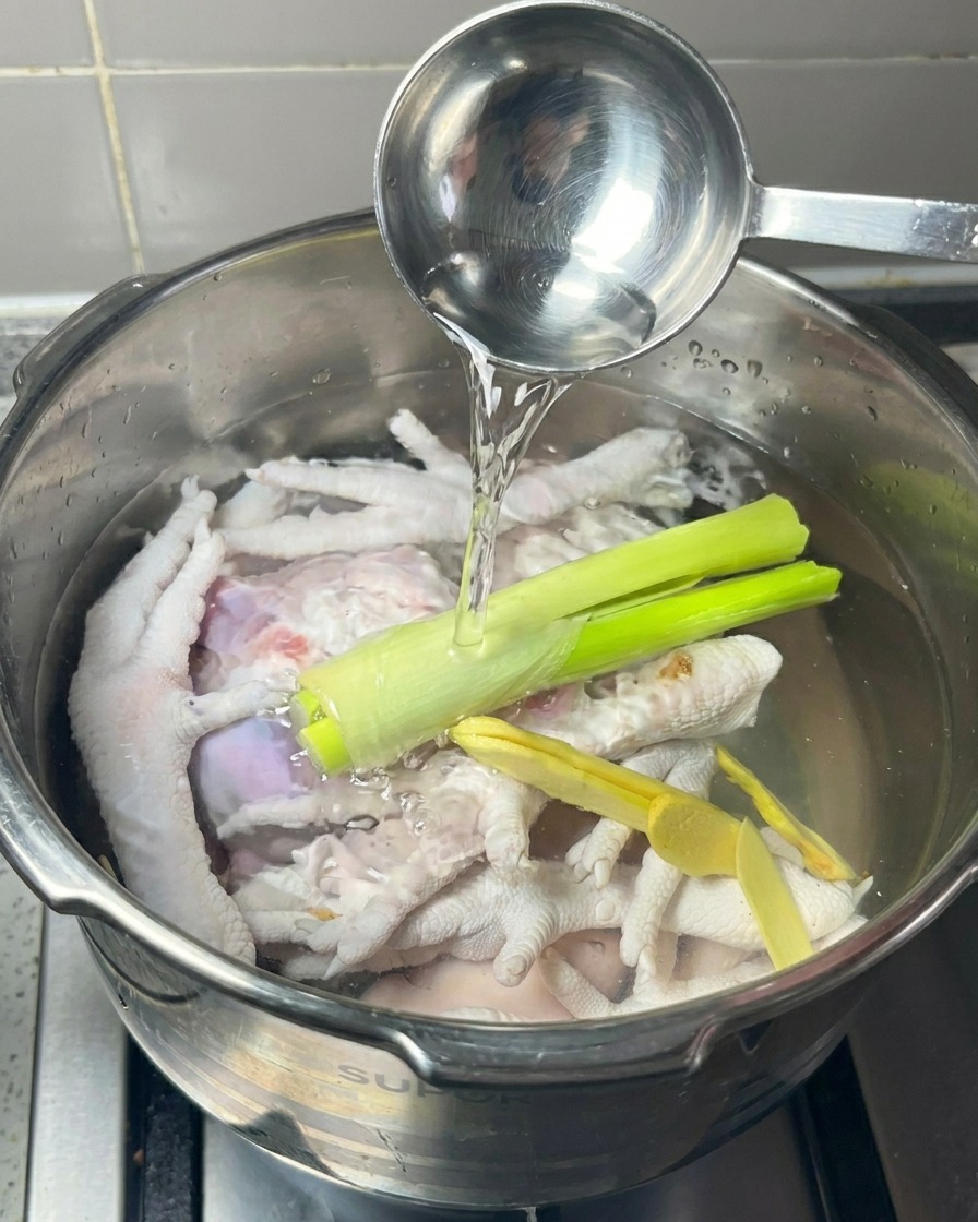 Du vin blanc versé à la louche dans un autocuiseur contenant des pattes de poulet, du gingembre et des oignons verts.