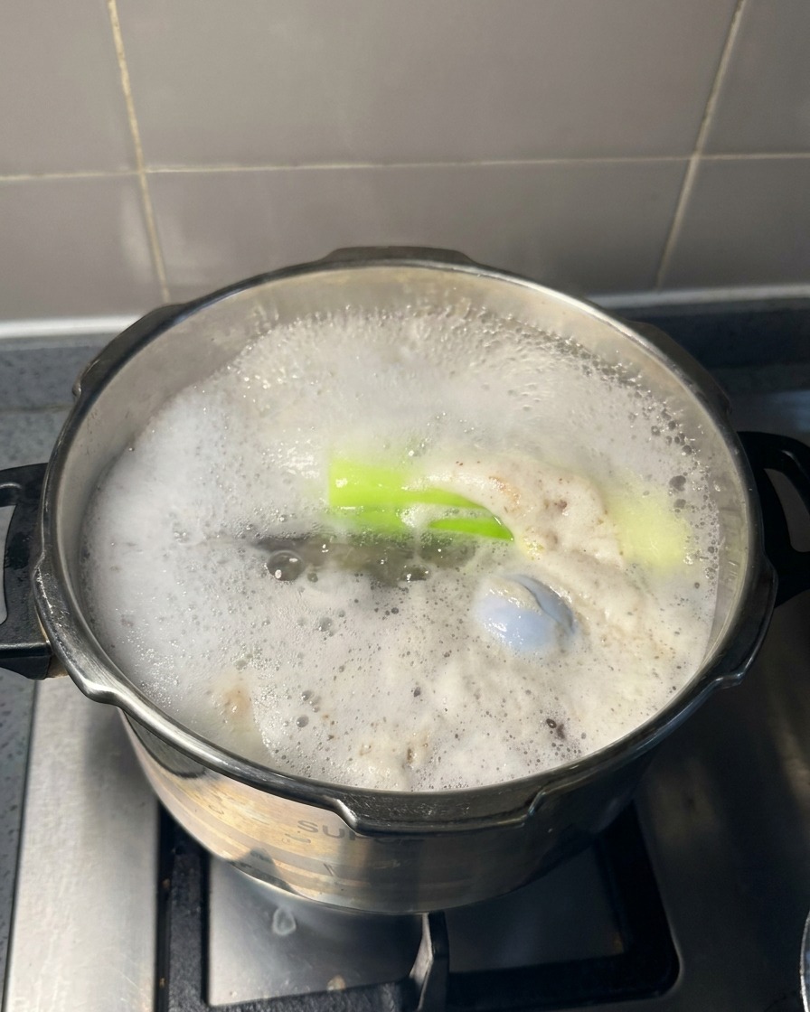 Une grande cuillère en métal retirant la mousse grise à la surface dun bouillon en ébullition.