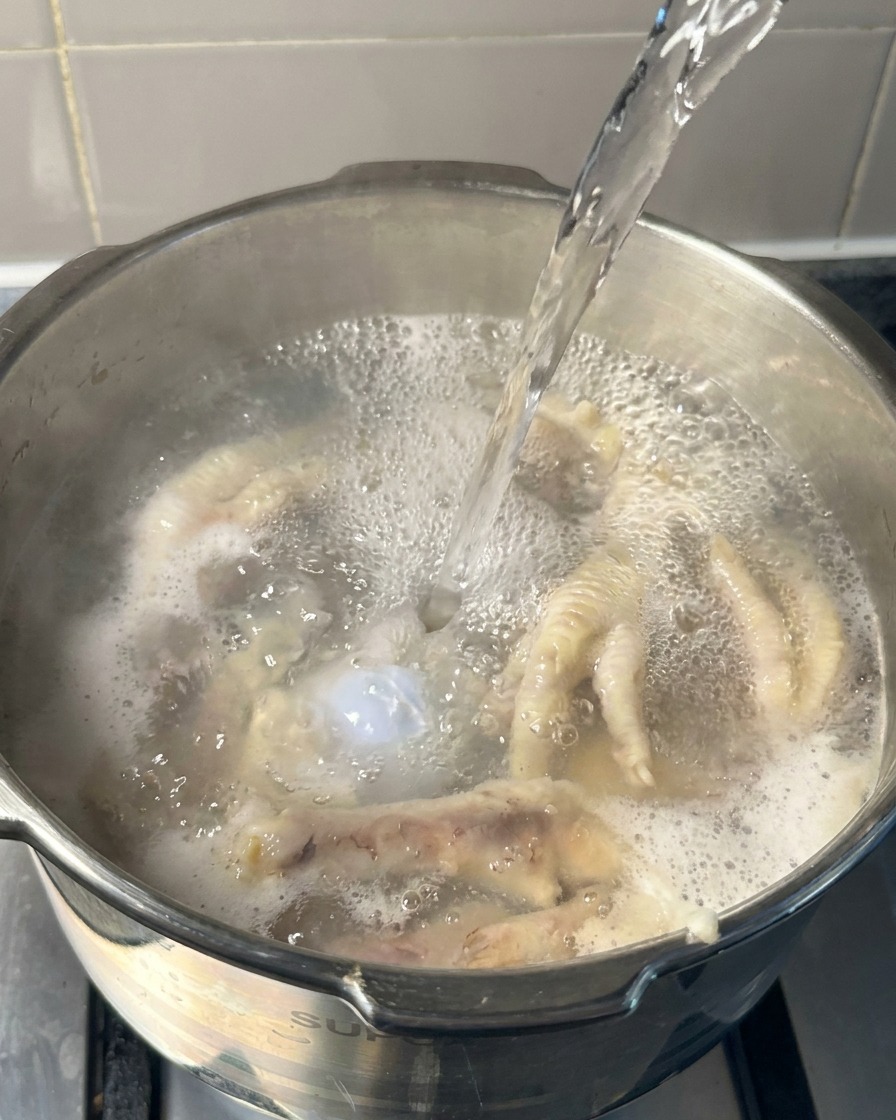 De leau bouillante versée dans une marmite contenant des os et des pattes de poulet précuits.