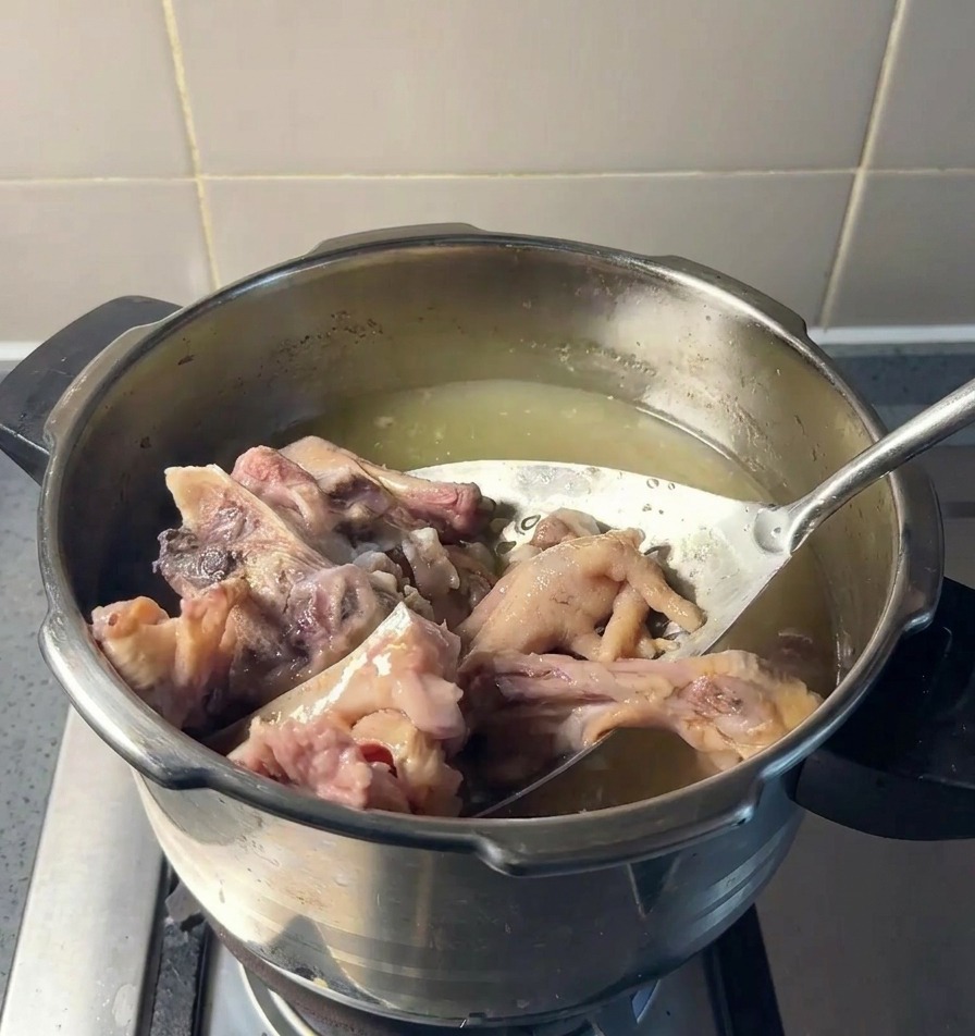 Une écumoire soulevant des morceaux dos et de pattes de poulet hors dun bouillon jaunâtre.