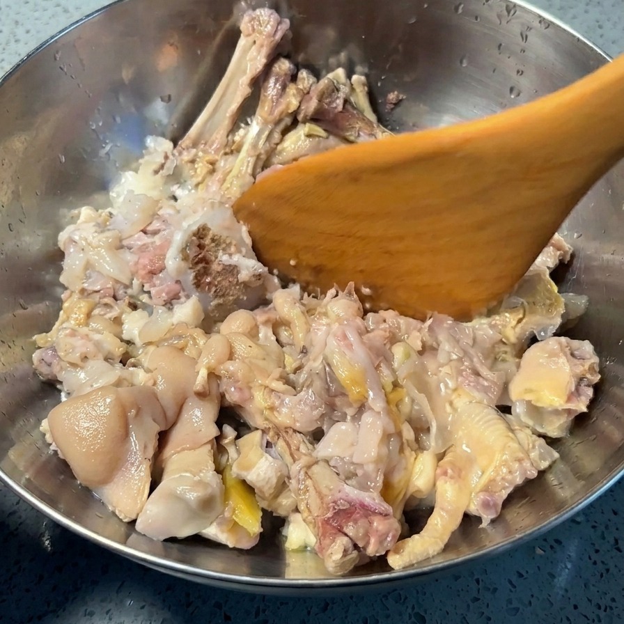Une spatule en bois pressant les pieds de porc et les pattes de poulet dans un bol en inox pour séparer la chair des os.