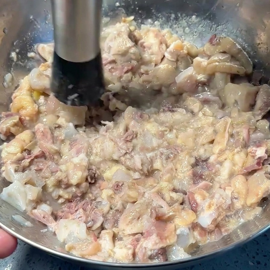 Un presse-purée écrasant la viande de porc et de poulet cuite au fond dun bol en inox.