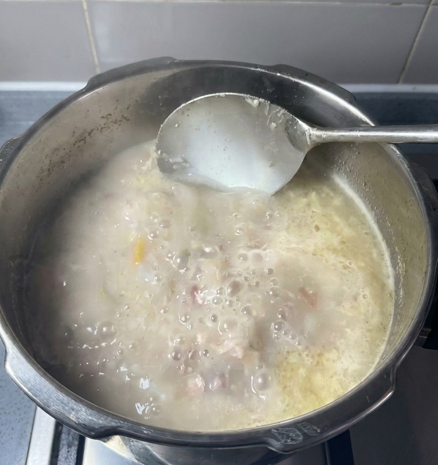 Une louche mélangeant un bouillon opaque blanc ivoire où tourbillonnent des morceaux de viande fondante.