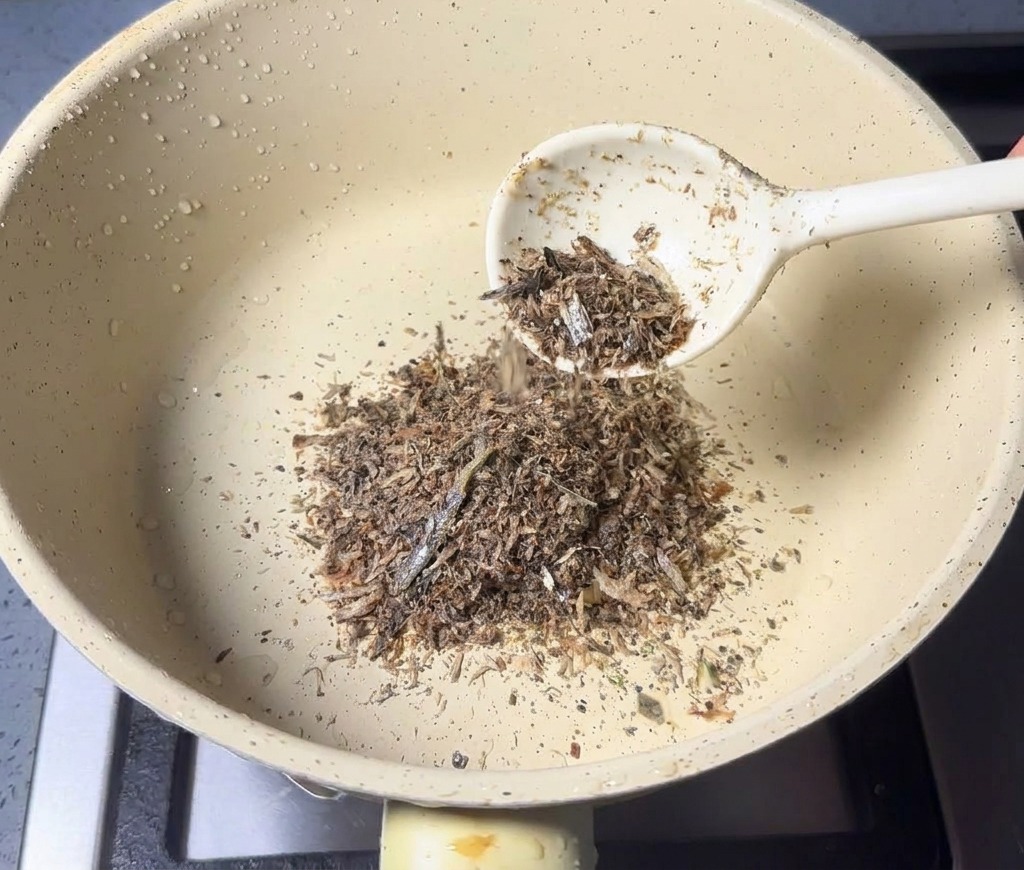 Une cuillère de poudre de fruits de mer ajoutée dans une casserole claire et sèche.