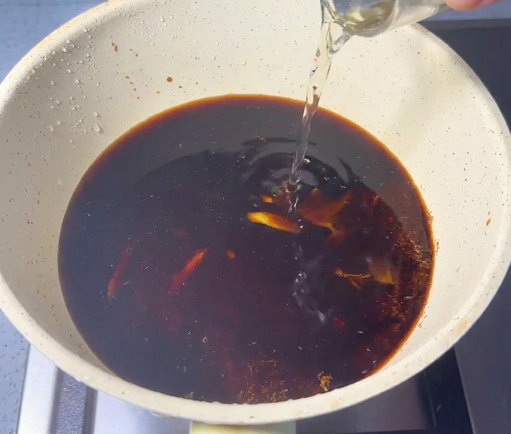 Liquide clair versé dun verre dans une casserole contenant la sauce soja et la poudre de poisson.