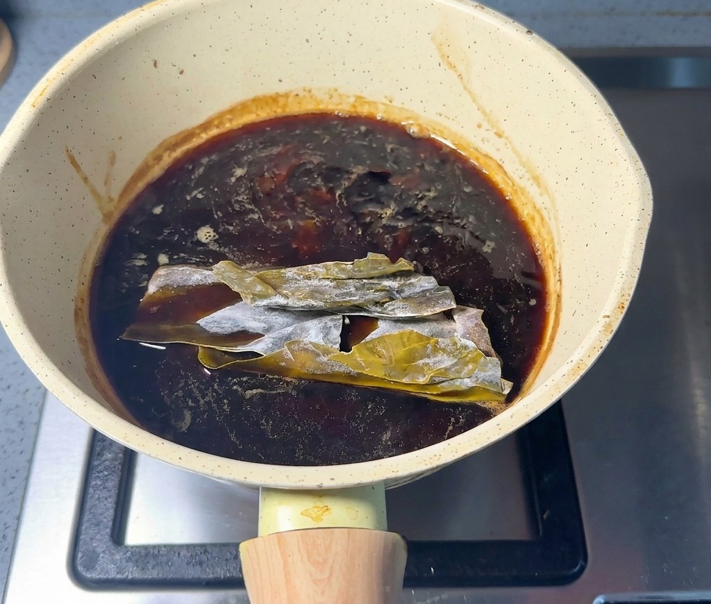 Feuilles de kombu séché immergées dans la sauce dassaisonnement sombre dans une casserole.