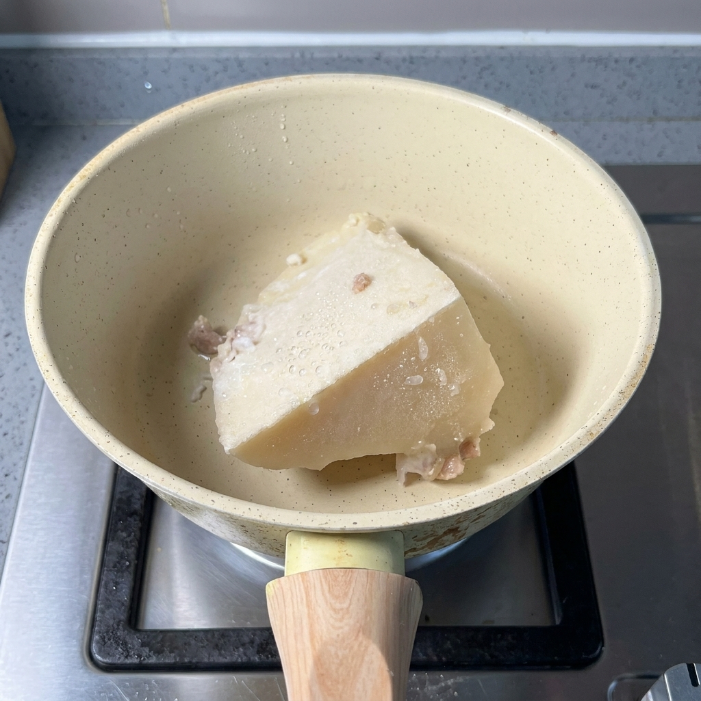 Un bloc de bouillon dos de porc congelé et une cuillère de poudre de poisson dans une casserole.