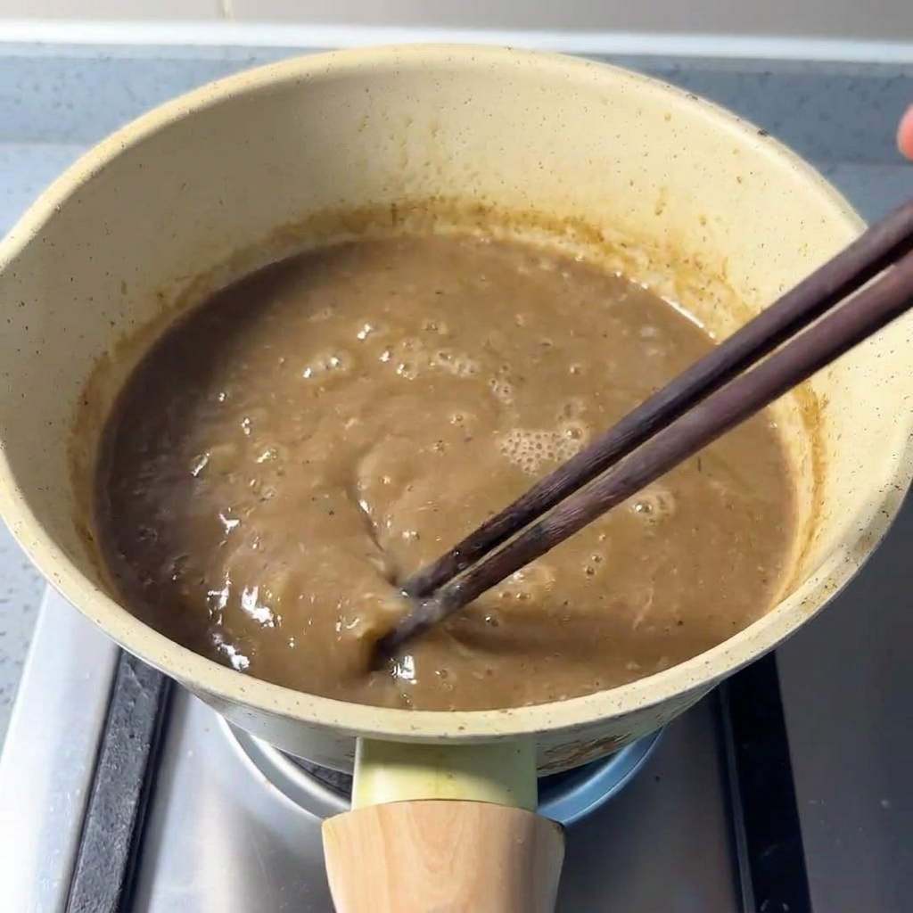 Mélange dun bouillon de porc épais et brunâtre avec des baguettes dans une casserole.