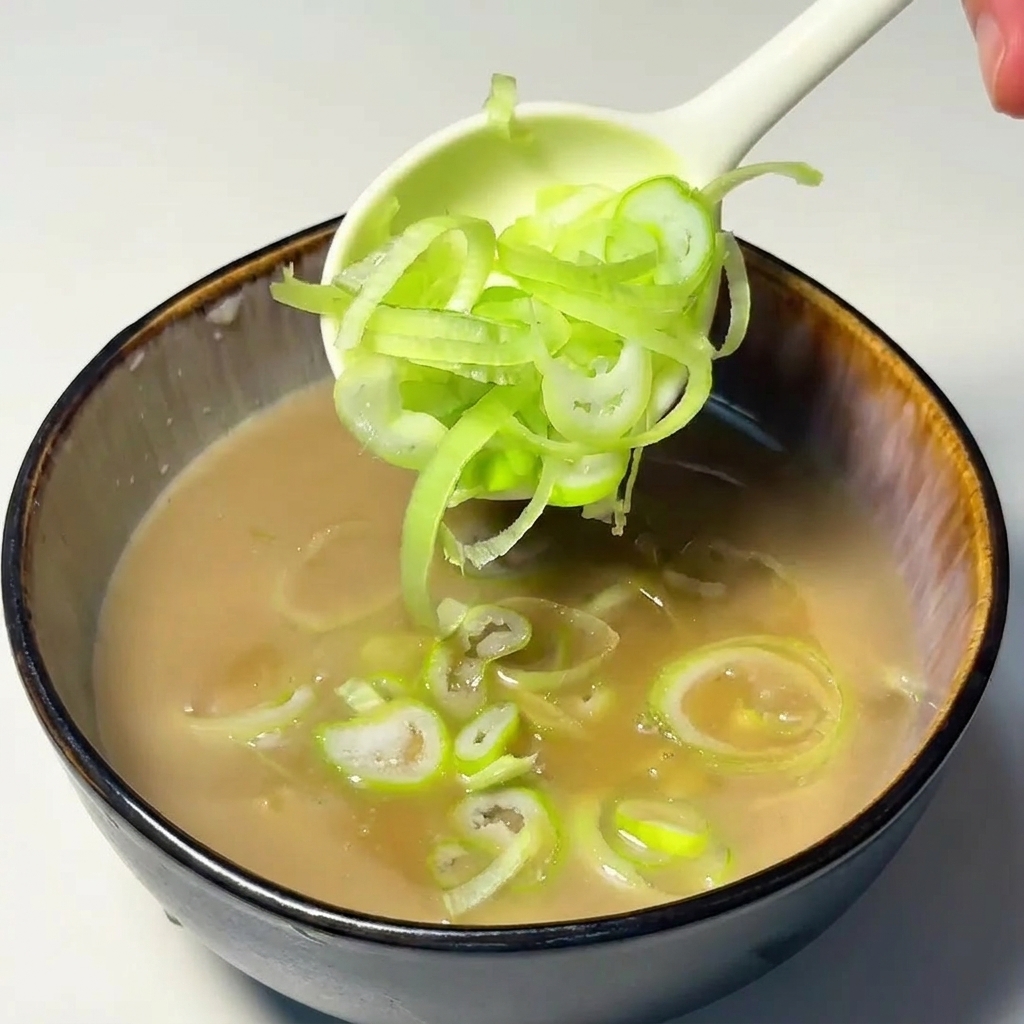 Une cuillère déposant des rondelles doignons verts frais dans le bouillon de trempage.