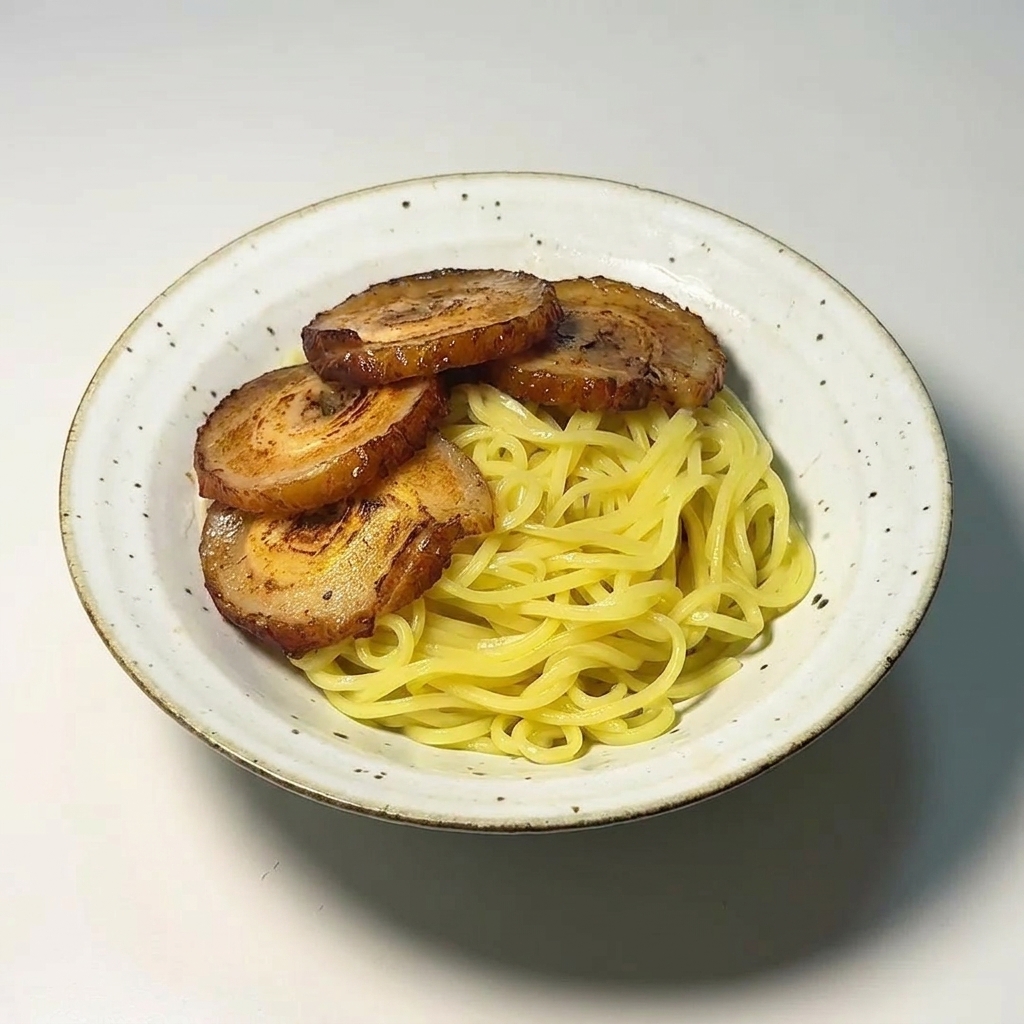 Quatre tranches de porc chashu grillé disposées sur un lit de nouilles ramen jaunes.