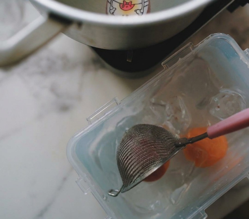 Une écumoire sortant un œuf bouilli dune casserole pour le placer dans un récipient deau glacée.