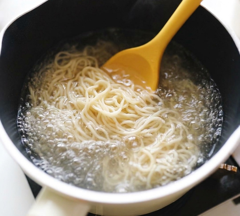 Nouilles ramen remuées avec une cuillère jaune dans une casserole deau bouillante.