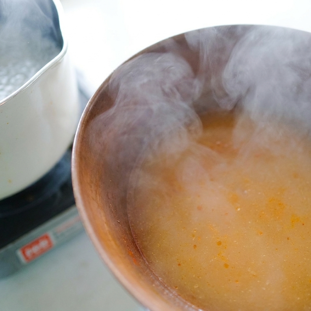 Eau de cuisson des nouilles versée avec une louche dans un bol contenant la pâte de miso.