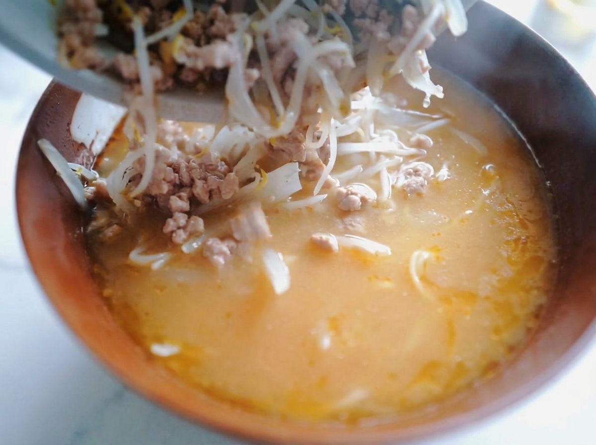 Une cuillère déposant le mélange de porc et de pousses de soja sur les nouilles dans le bouillon miso.