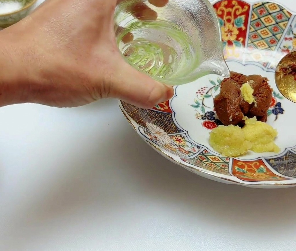 De lhuile neutre versée depuis un petit pichet en verre sur le mélange de miso et de gingembre.