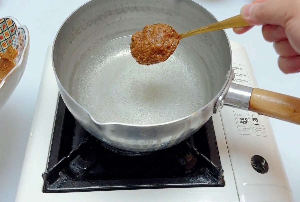 Une cuillerée de base de miso maintenue au-dessus dune casserole deau sur un réchaud.
