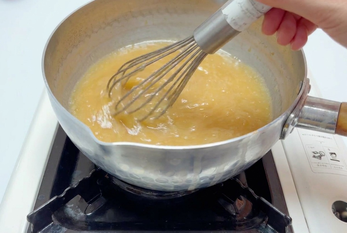 Un fouet métallique mélangeant un bouillon brun clair dans une casserole jusquà dissolution complète.