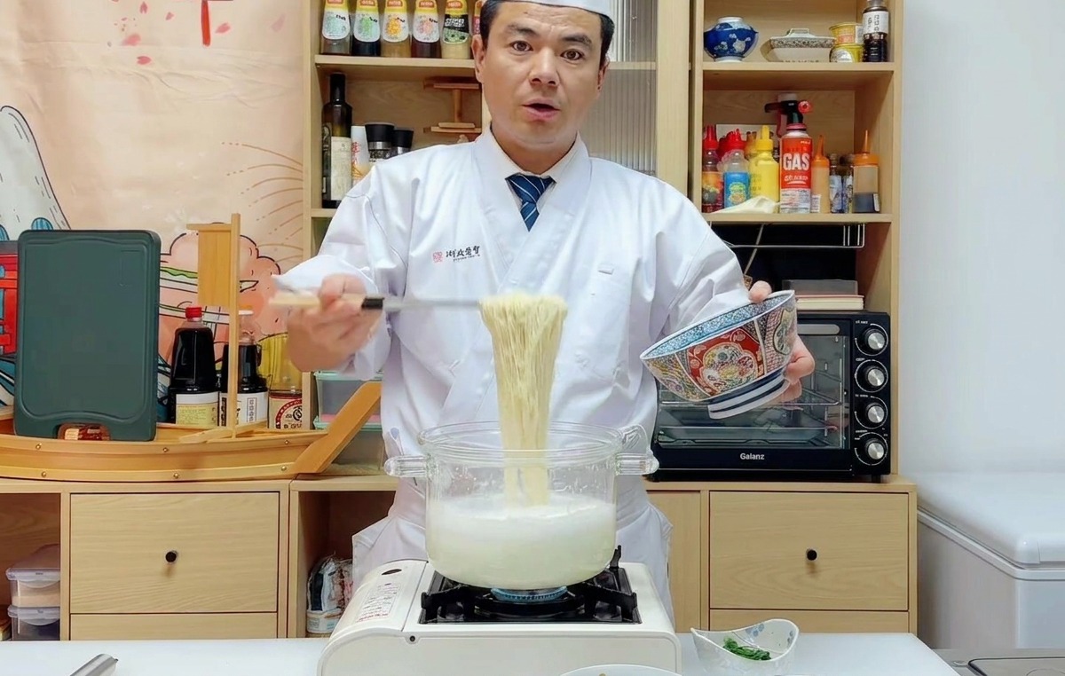 Le chef soulevant des nouilles cuites avec une passoire pour les placer dans un bol de service.