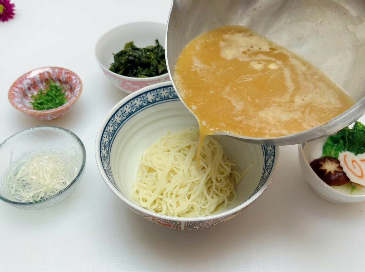 Bouillon miso bien chaud versé depuis une casserole sur les nouilles dans un bol en céramique.