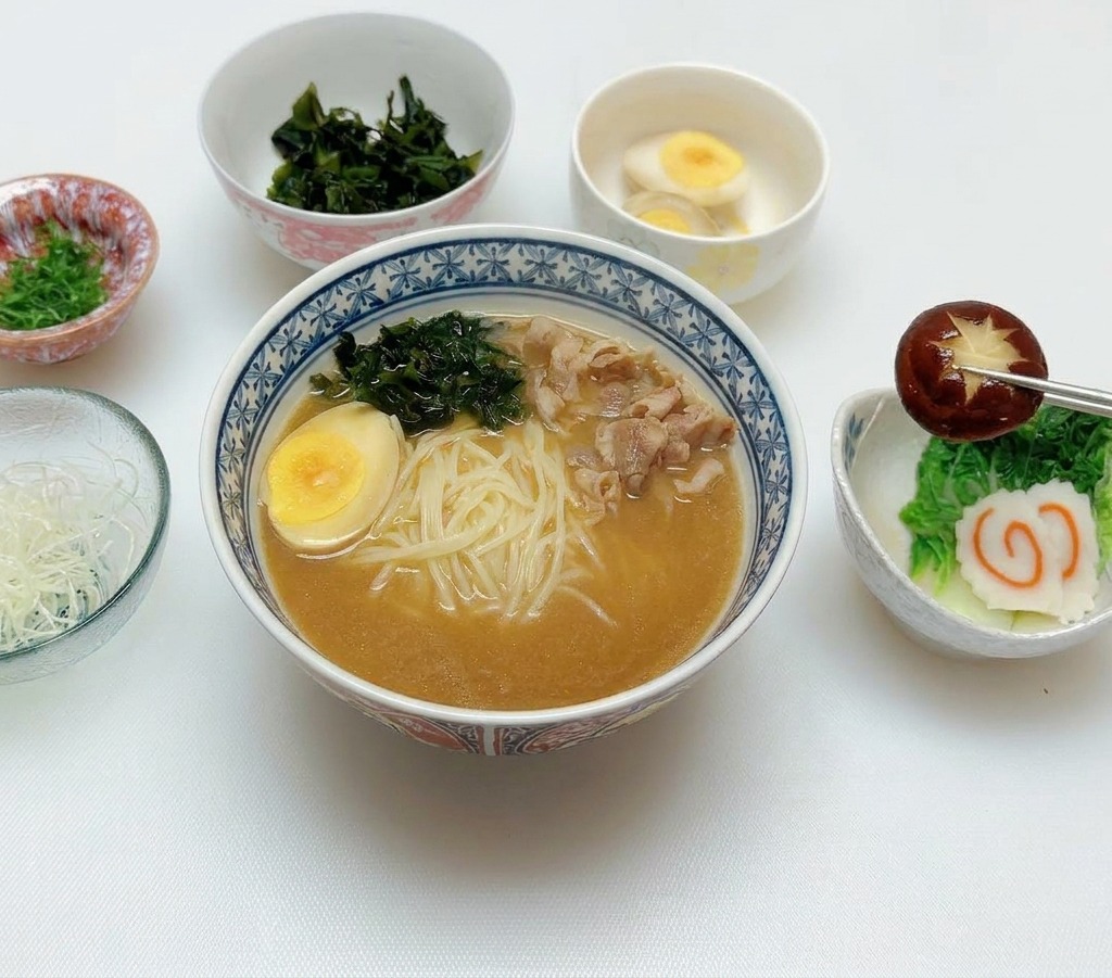 Des baguettes déposant un champignon shiitake sur les garnitures du bol de ramen.
